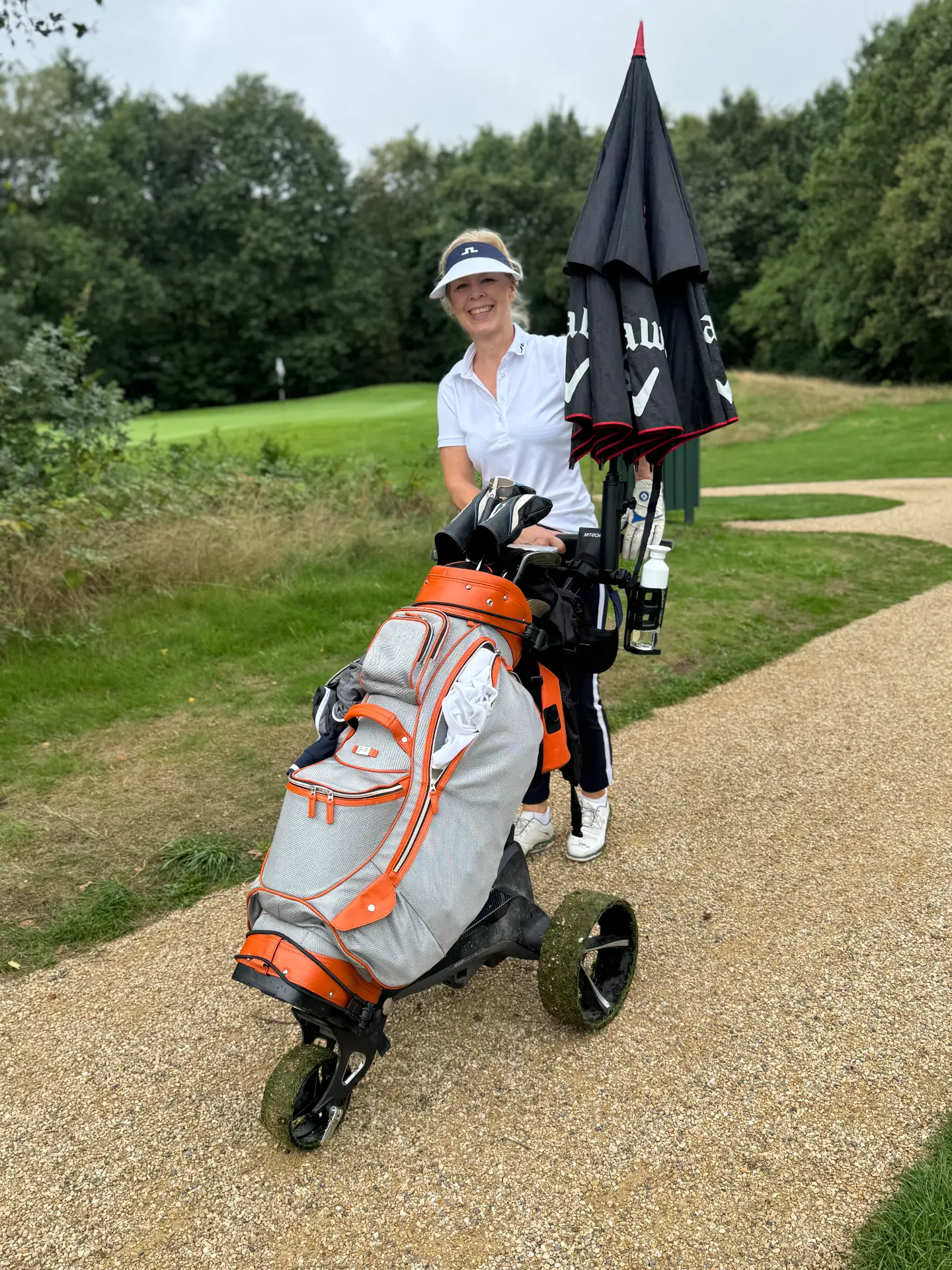Deelneemster met oranje golftas en trolley op het pad