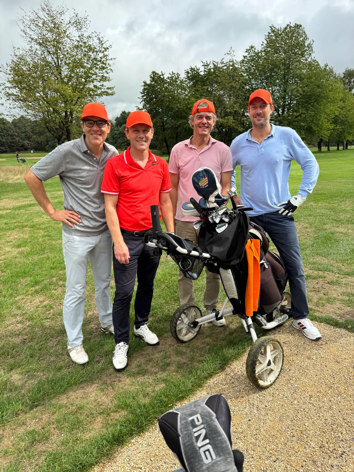 Vier deelnemers met oranje petten bij hun golftassen