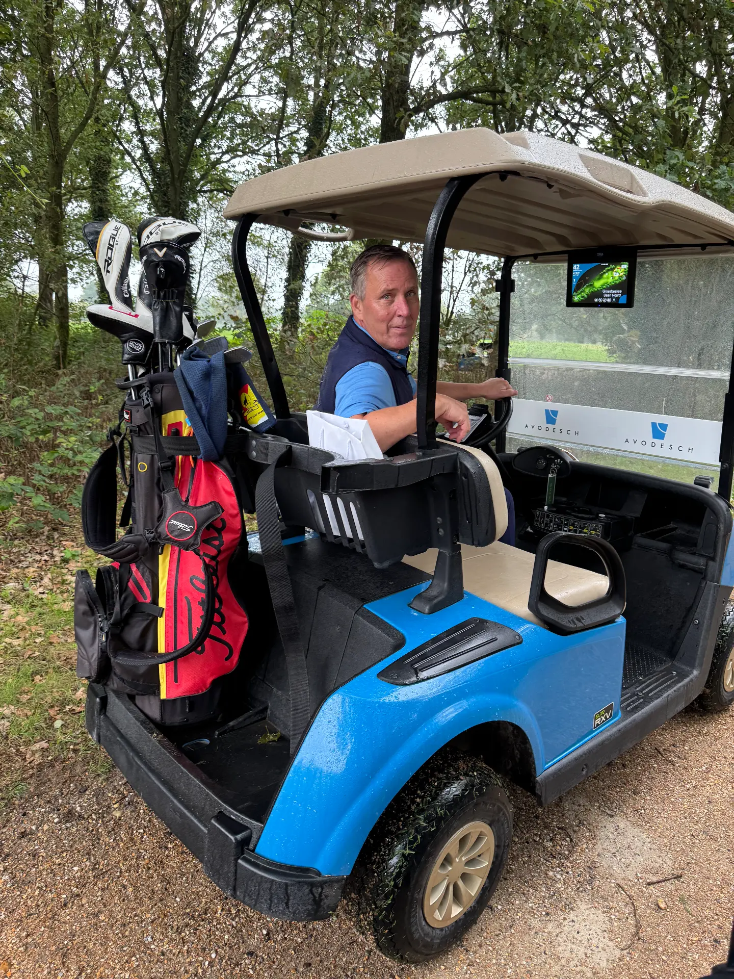 Deelnemer in blauwe golfkar met tassen