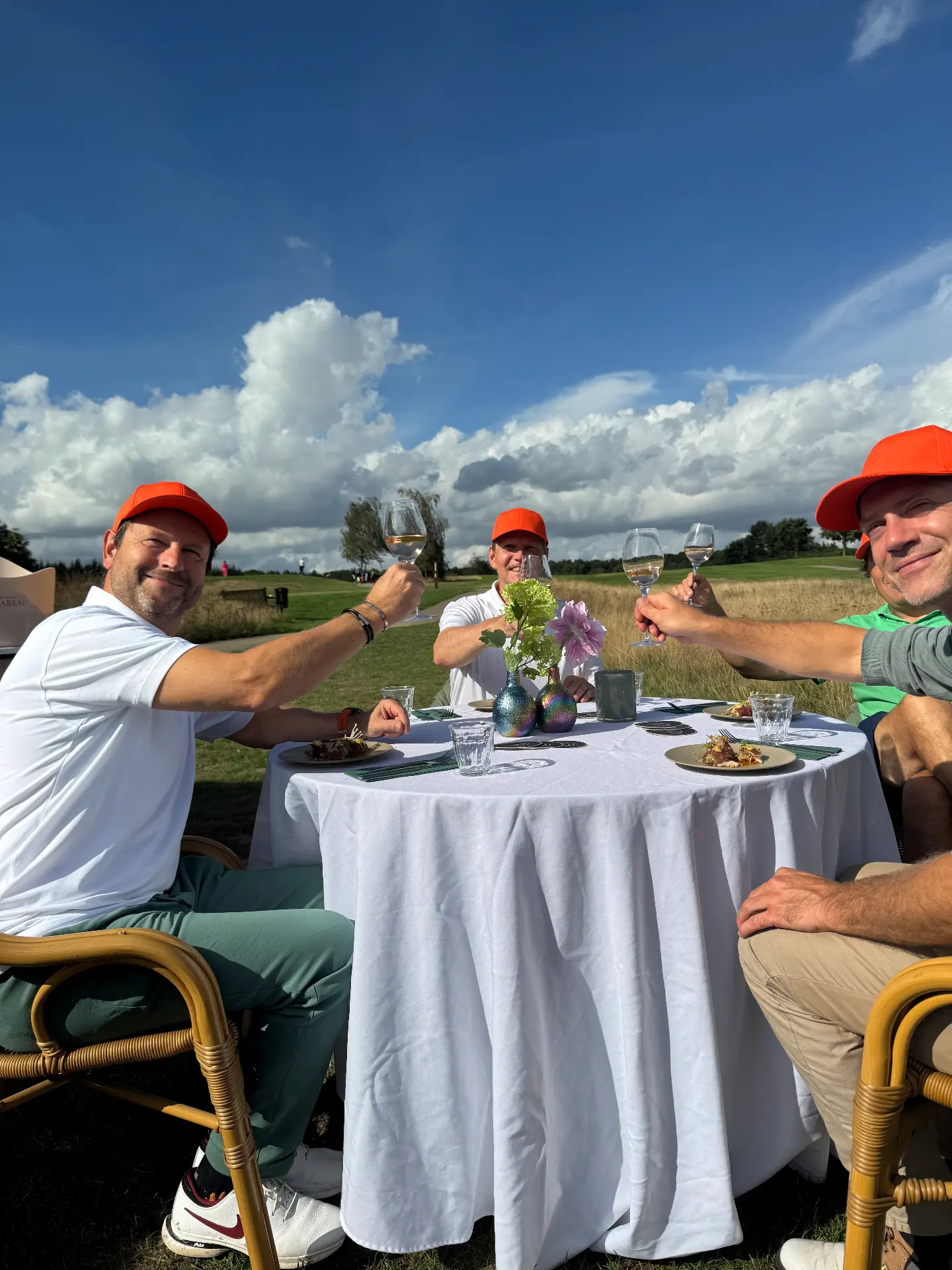 Drie deelnemers proosten aan een gedekte tafel in het veld